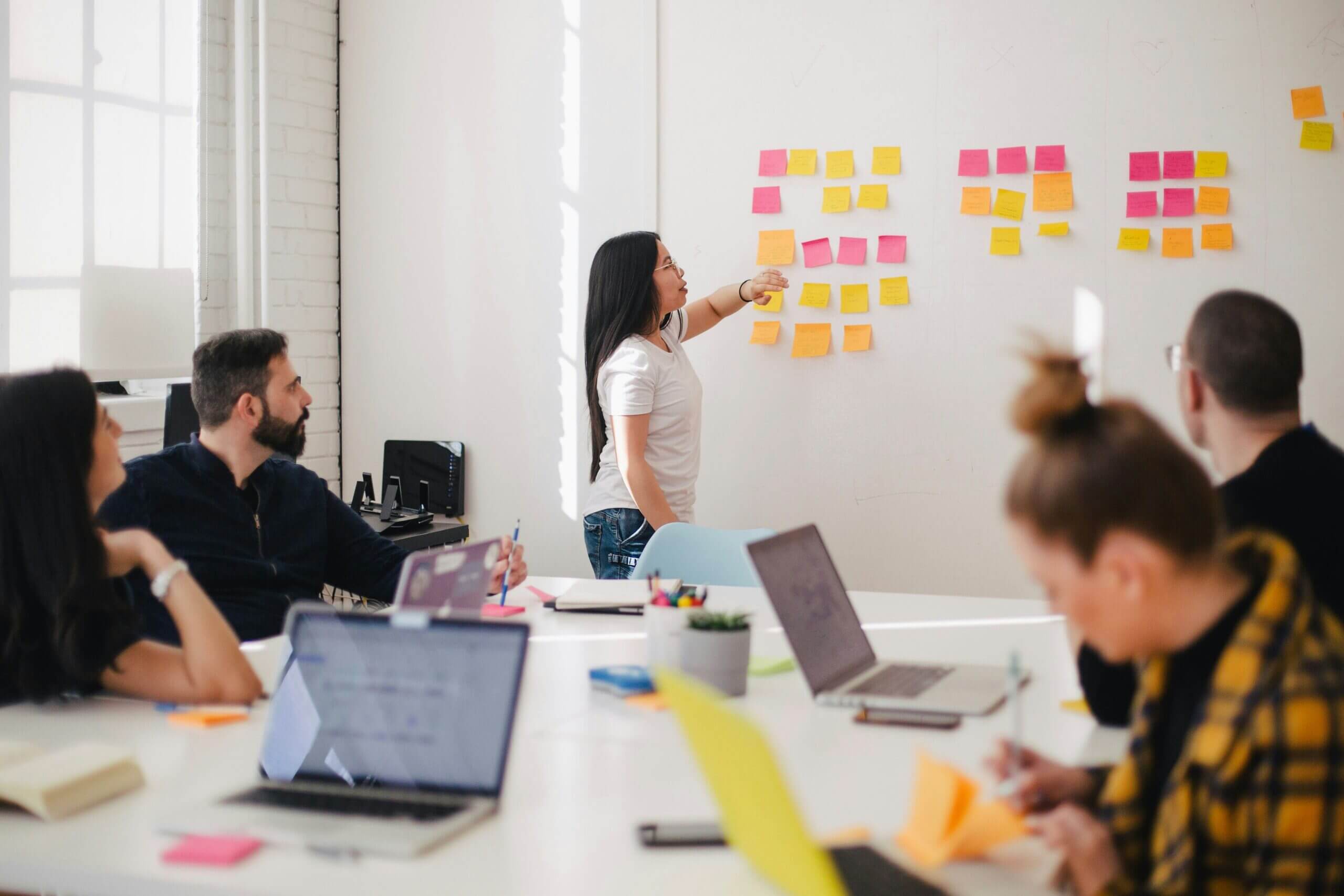 Team meeting with person pointing at colorful sticky notes on wall while others observe