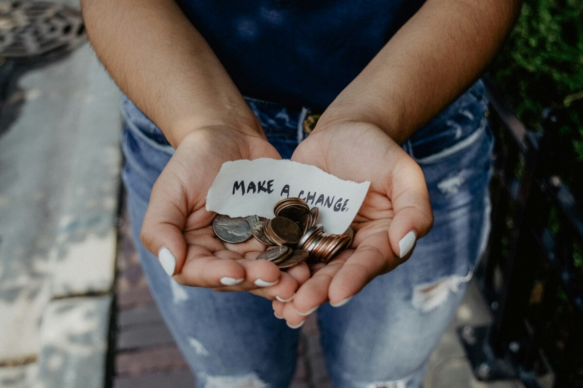 Hands holding coins and note reading 'make a change' in casual perspective