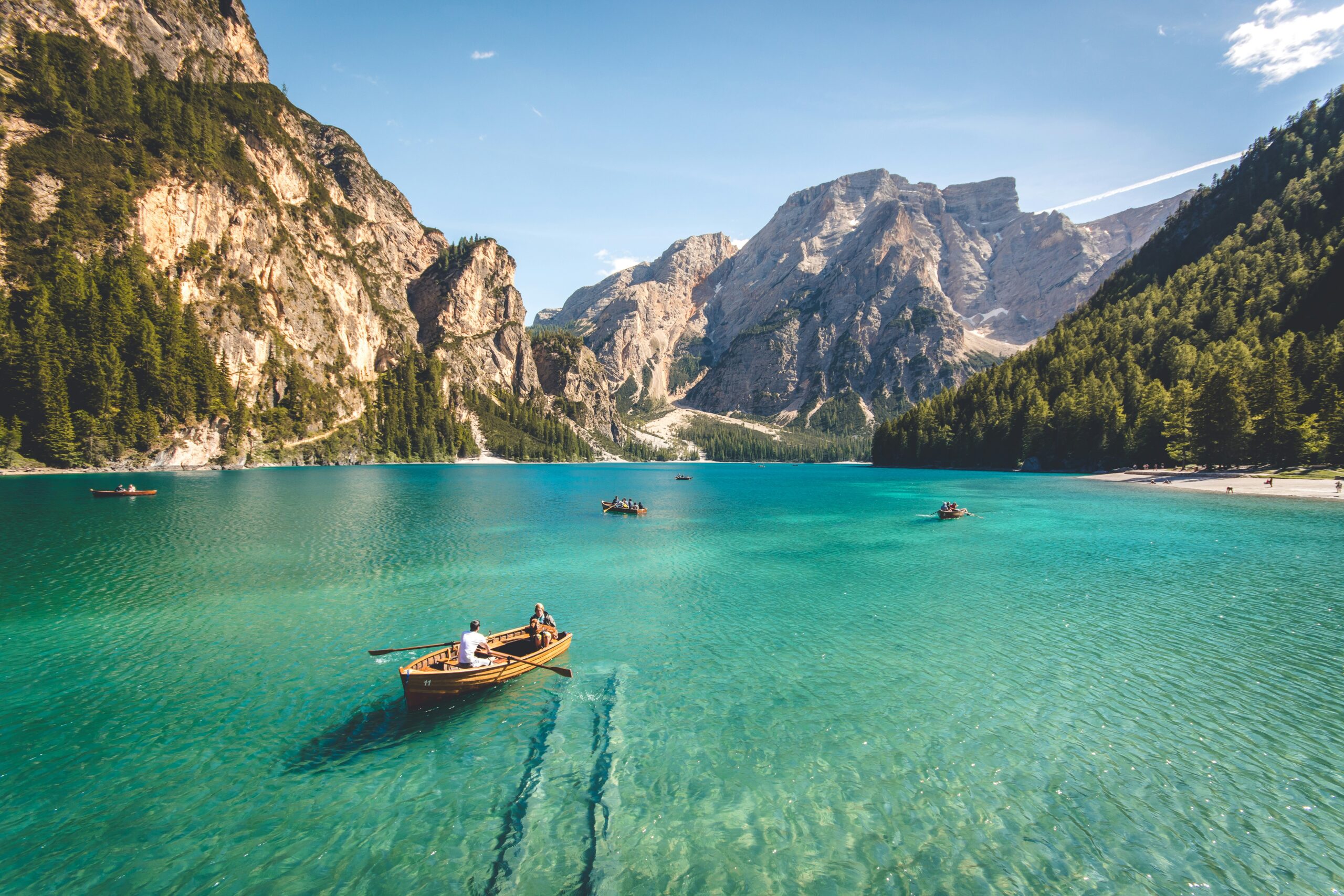 Boats on turquoise alpine lake surrounded by steep mountain peaks and forest