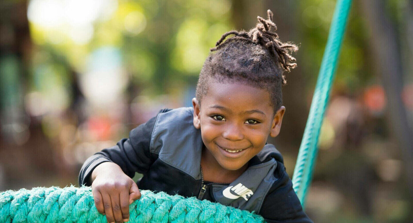 Young child smiling while leaning on turquoise rope, wearing black