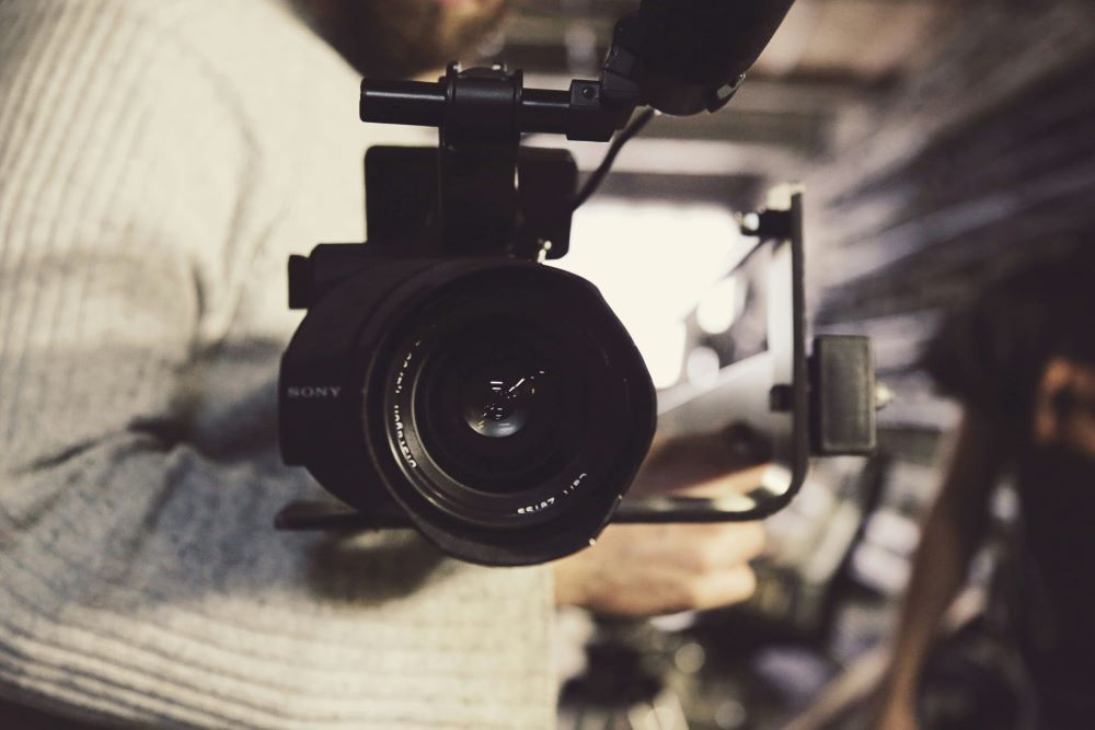 Close-up of a Sony professional video camera lens mounted on a stabilizing rig, with soft background bokeh